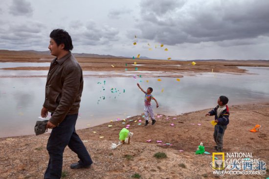在中国沙漠化日益严重的青海省，藏族男孩在佛教仪式上向黄河水中撒入纸片。